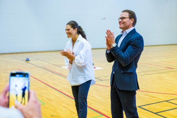 Kronprinsessan Victoria och Prins Daniel besökte Fritidsbanken Sigtuna och Steningehöjdens skola 7 september 2022. Foto: PELLE T NILSSON/Swedish Press Agency. På bilden syns Kronprinsessan och Prinsen i en sporthall där de ler.