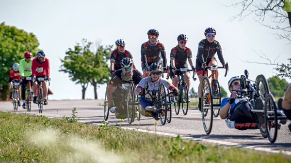 Flera cyklister cyklar på en väg. Det är handcyklister och andra cyklister.